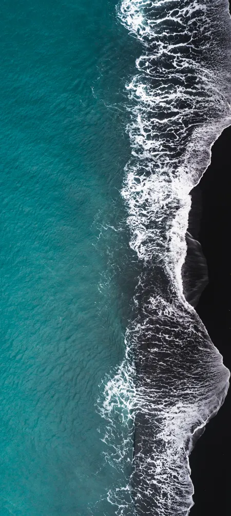 Aerial view of waves on black sand beach.
