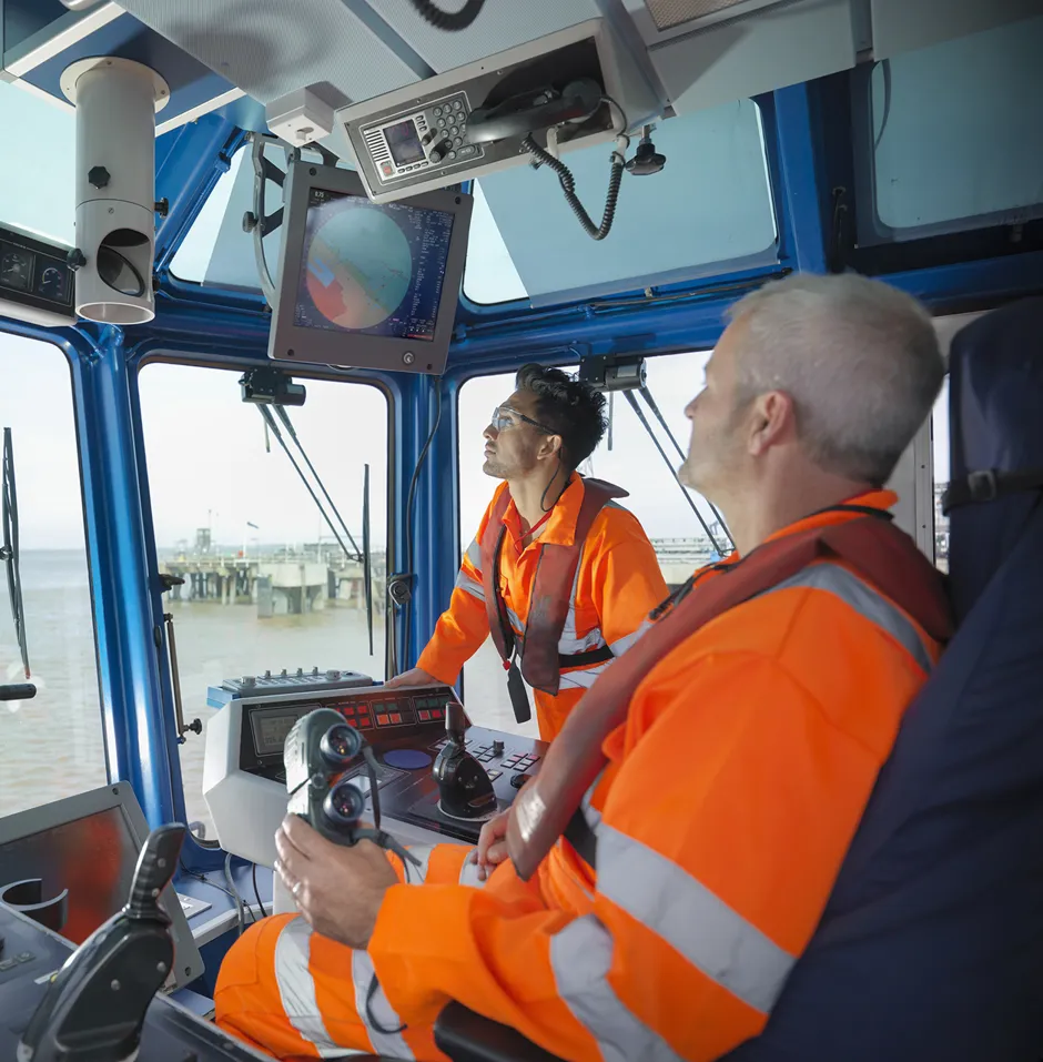 Tug workers wearing protective clothing steering tug
