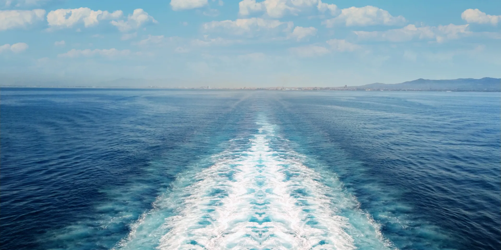 Blue ocean with white wake and scattered clouds.