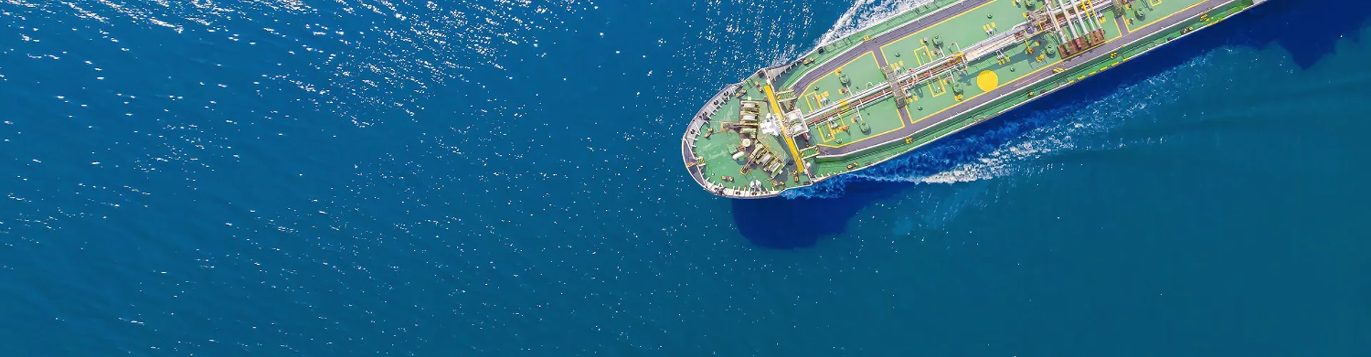 Aerial view of a large ship navigating through deep blue water, with sunlight reflecting off the surface.