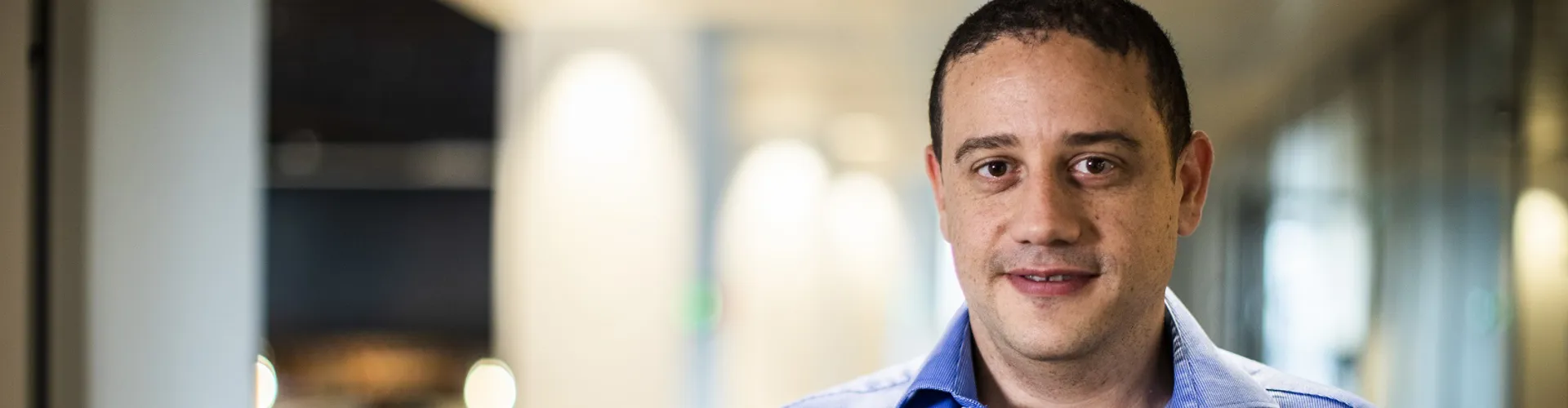 Man in a blue shirt standing in an office corridor.