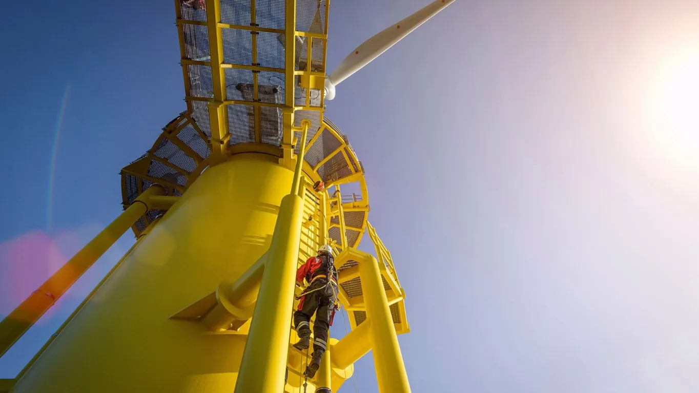 Person in safety gear climbing a bright yellow offshore wind turbine platform.