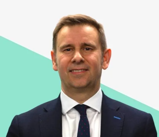 Man in a dark suit and tie, smiling at camera.