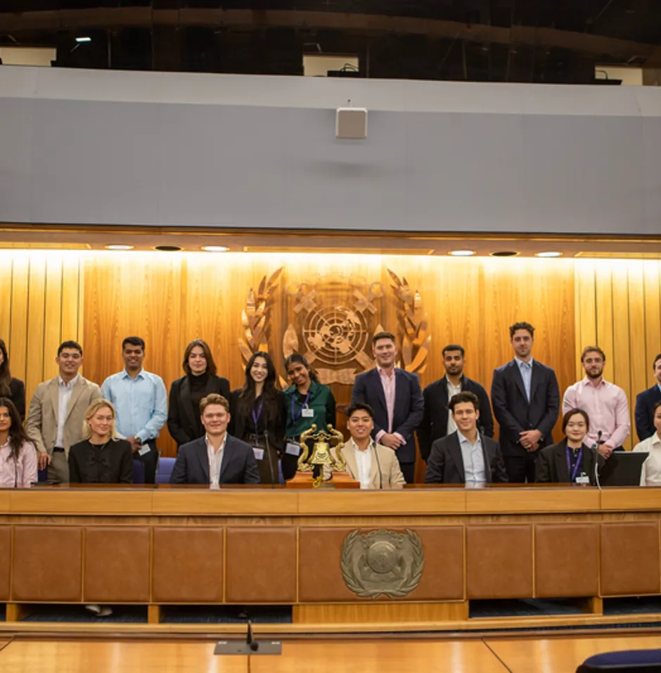 Group in business attire posing in a formal room with a United Nations emblem backdrop.