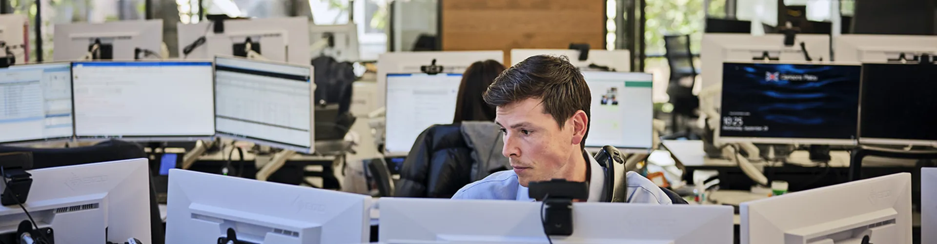 Office workspace with multiple screens and people.