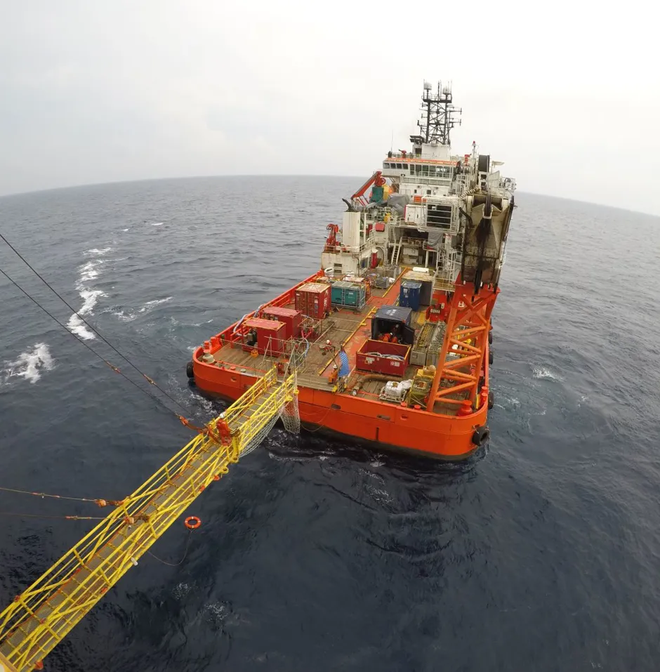 Orange supply ship in open ocean with loading platform.