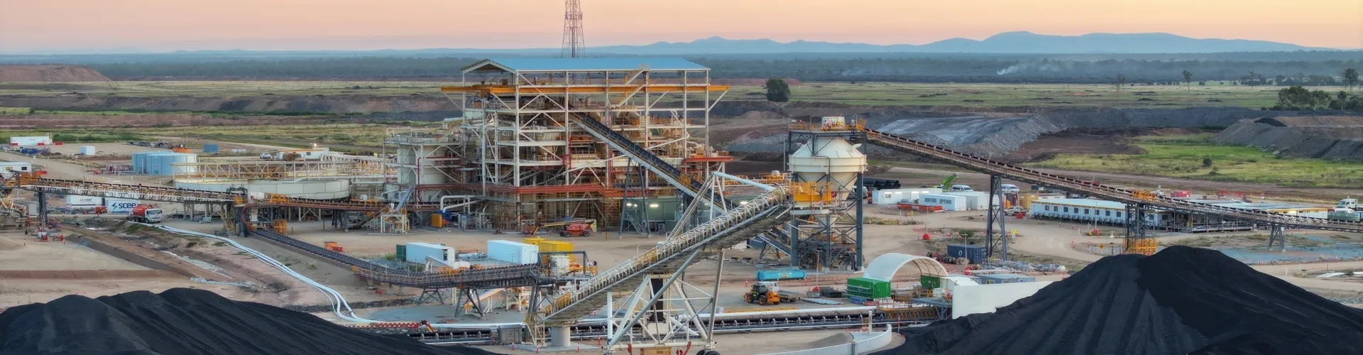 Coal processing facility with coal piles, conveyor belts, and machinery at sunrise.