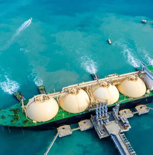 Aerial view of large LNG tanker with spherical tanks anchored near port.