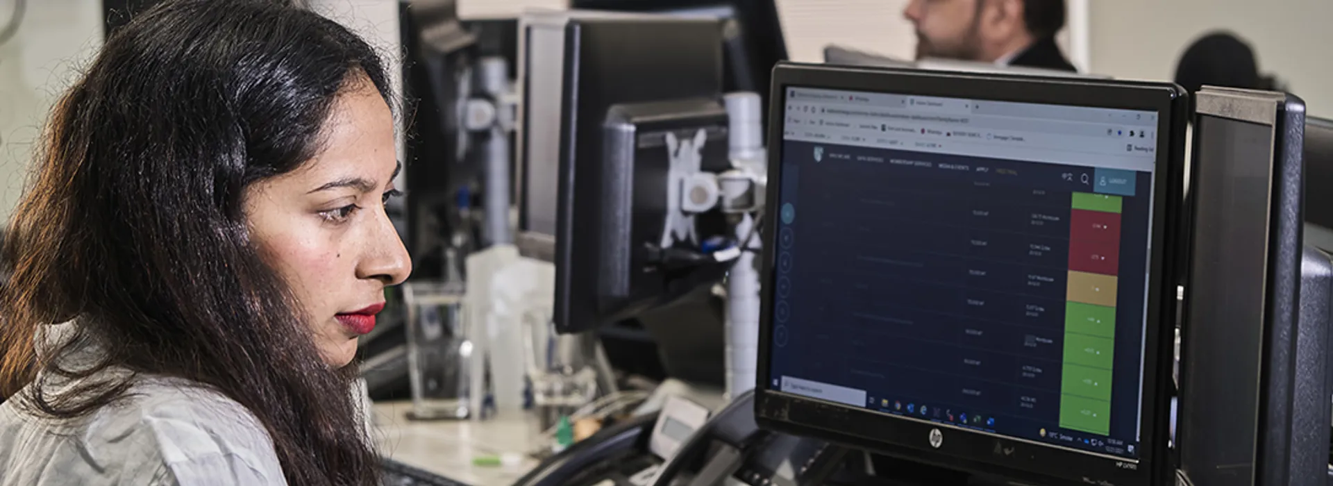 Woman with dark hair at a desk focused on multiple computer monitors with data.