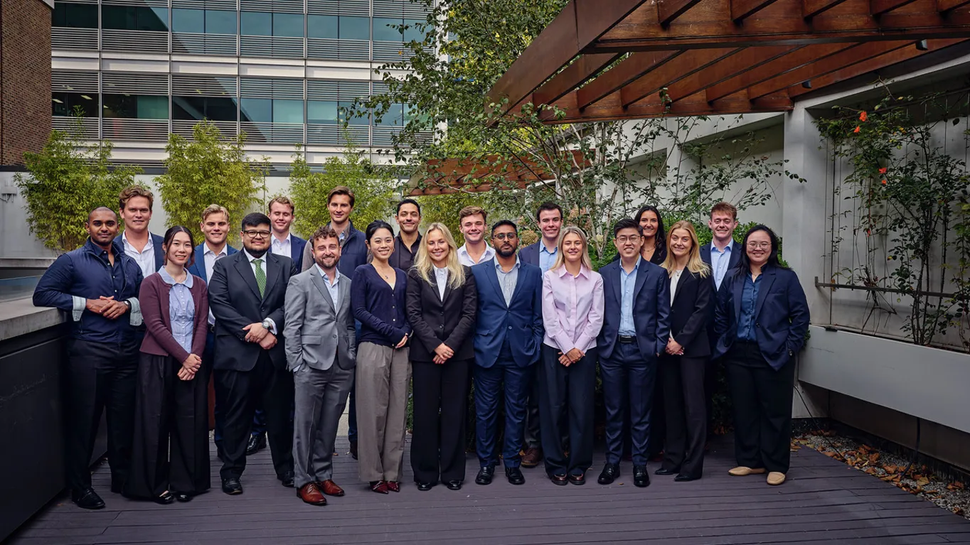 Group of 21 people in professional attire posing outdoors near a modern building.