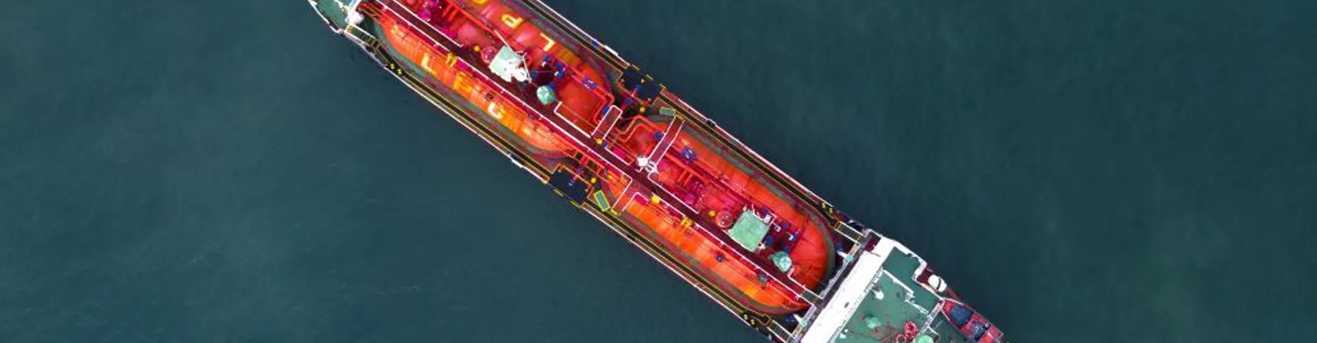 Aerial view of a large red and green cargo ship floating on calm blue water.
