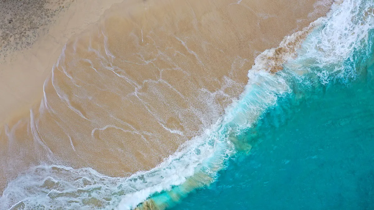 Aerial view of sandy shore meeting turquoise sea.