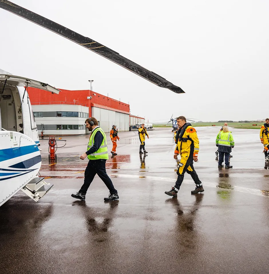 Helicopter crew in yellow suits walking on wet tarmac.