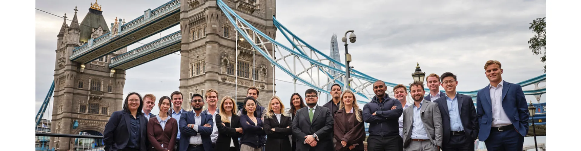 Diverse group of people in business and casual attire standing in front of Guyana's Tower Bridge.
