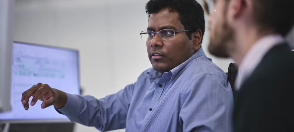 man talking to his colleague and pointing at his computer screen