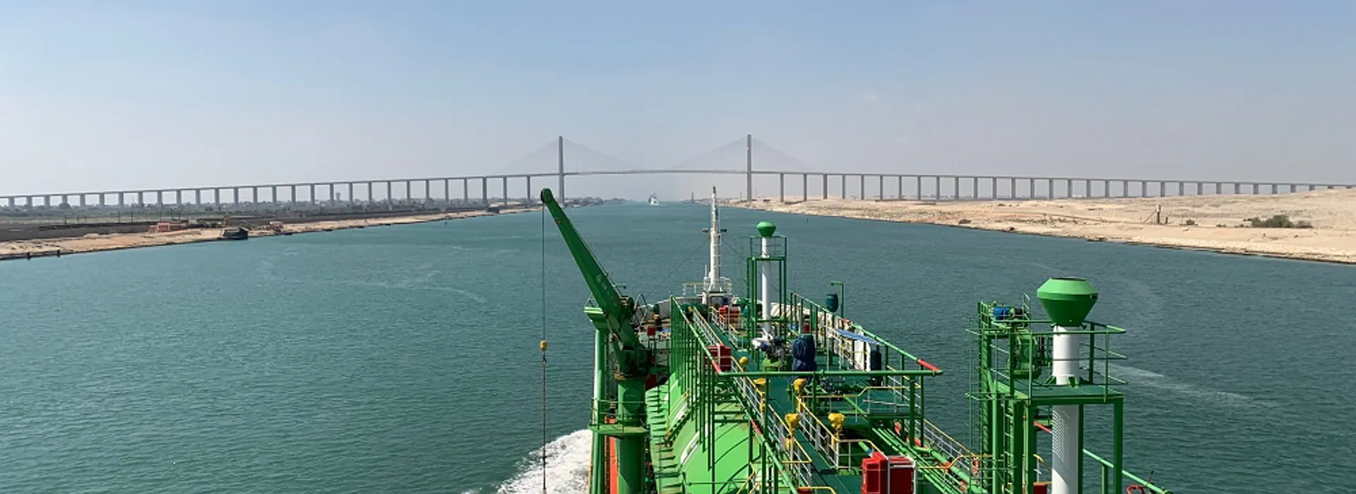 Green ship navigating a canal beneath a bridge.