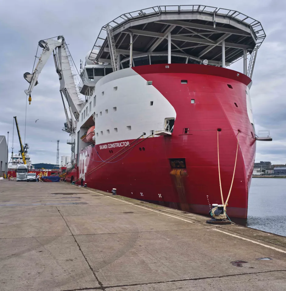 Large red ship docked at a port under cloudy skies.
