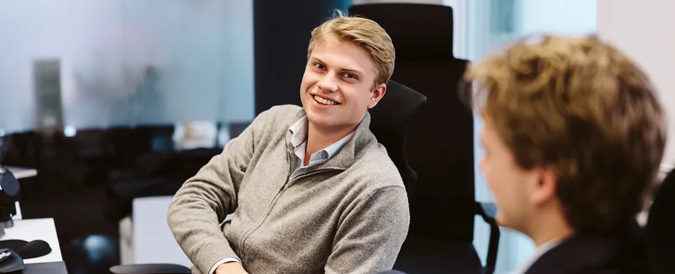 two men sitting at desk, talking