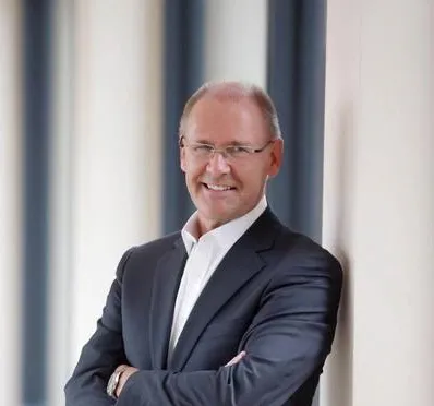 Smiling man in a suit leaning against a wall.