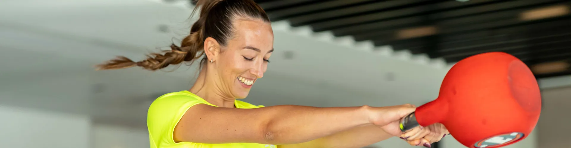 Woman in neon shirt swinging a kettlebell.