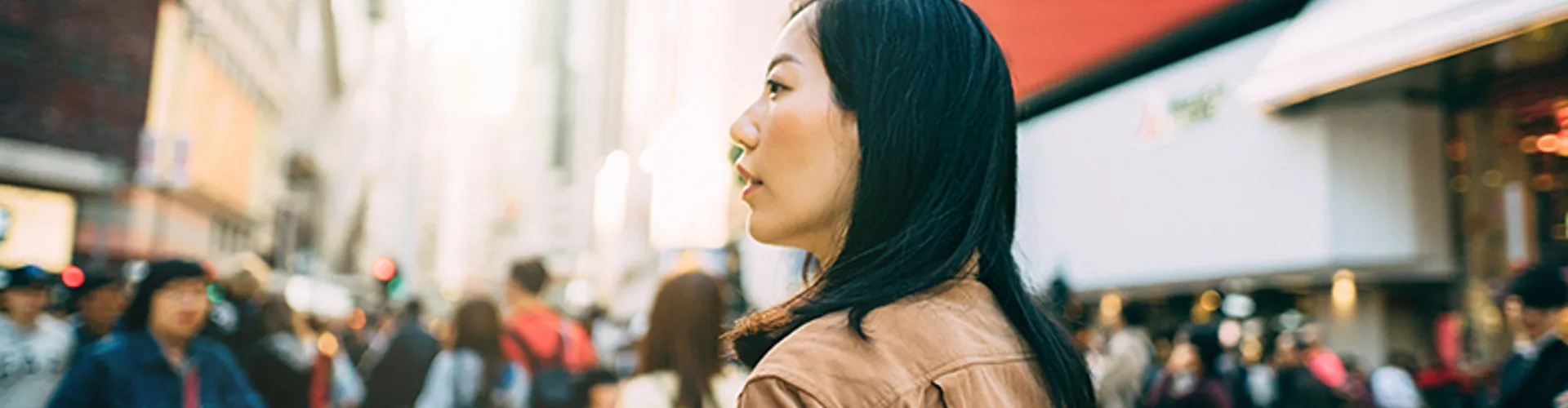Young woman checking on mobile phone while crossing street and commuting in busy downtown city street