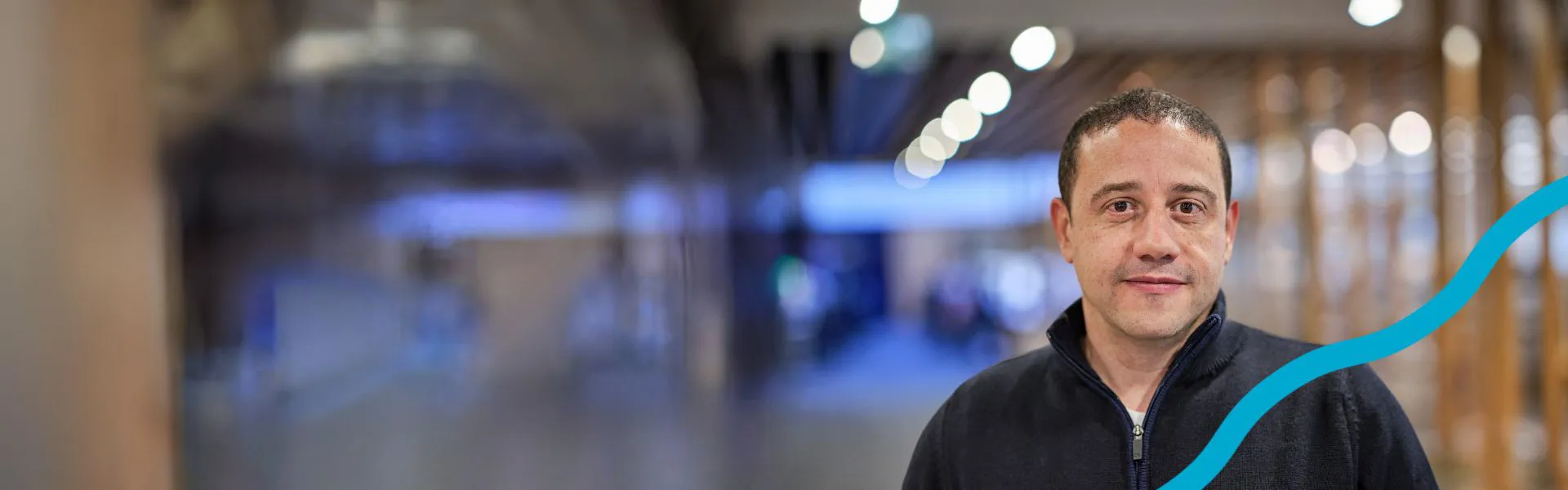 A person stands smiling in a blurred indoor space.