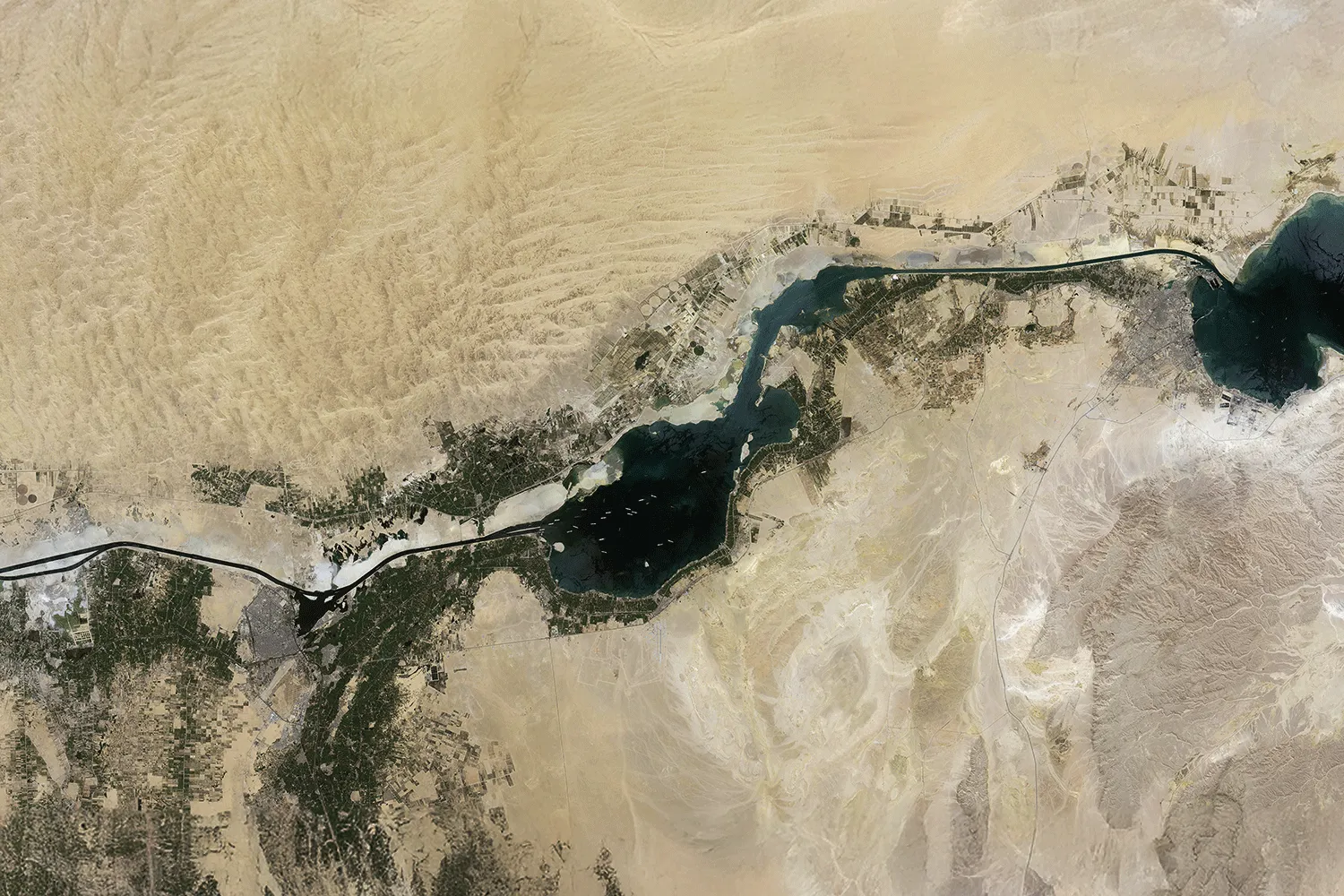 Aerial view of desert landscape intersected by a dark blue river with green agricultural land.