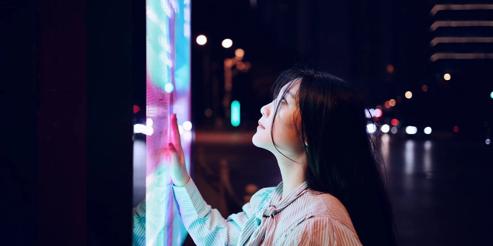 Woman touching a bright digital display at night.