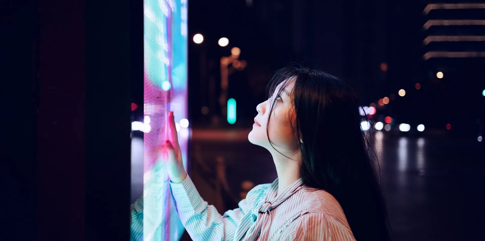 Woman touching a bright digital display at night.