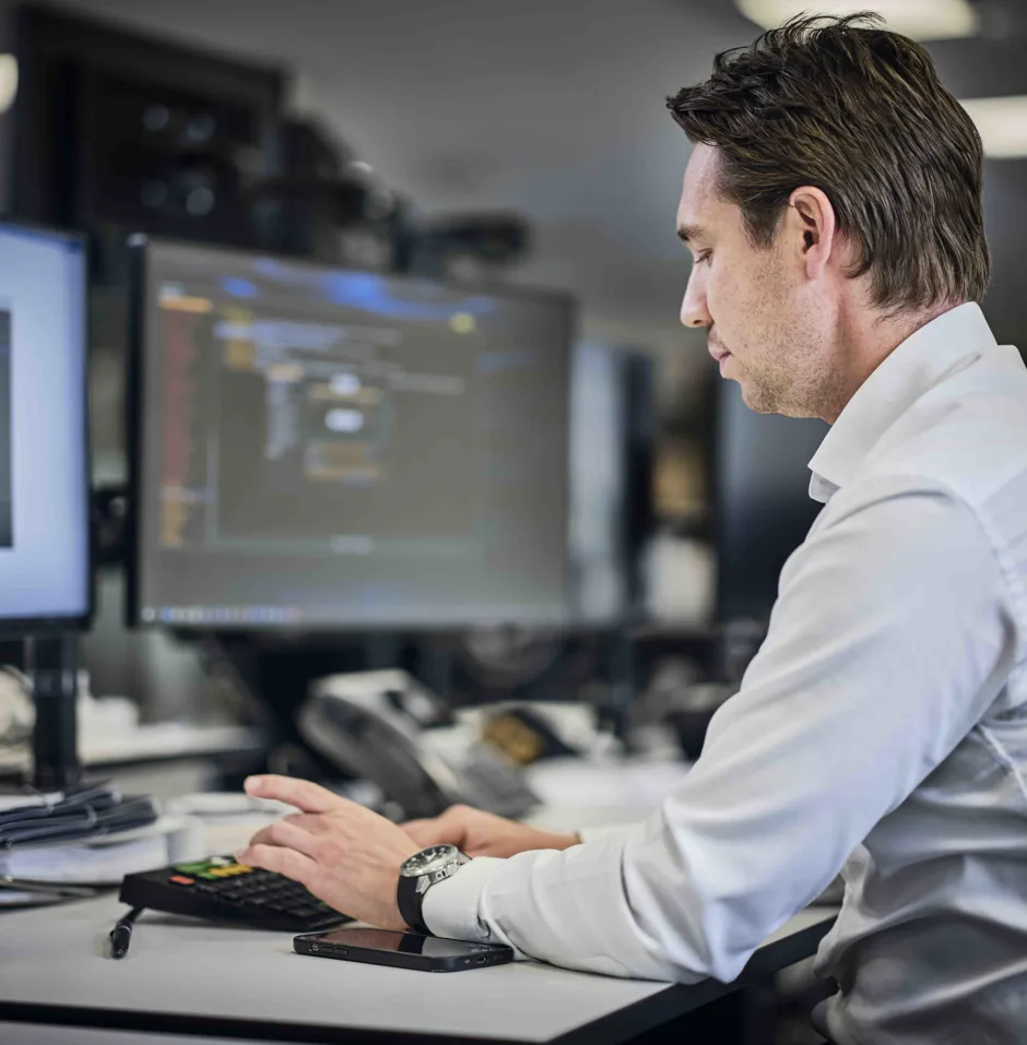 Man in light shirt focused on two monitors displaying code in a modern office.