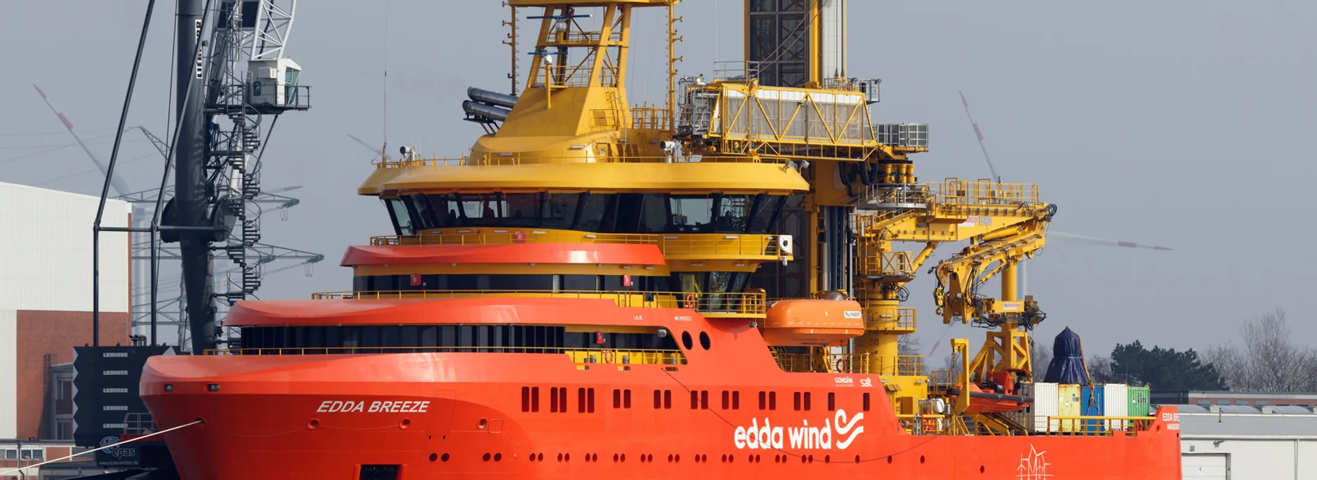 Large orange and yellow ship "Edda Breeze" docked at a port under an overcast sky.