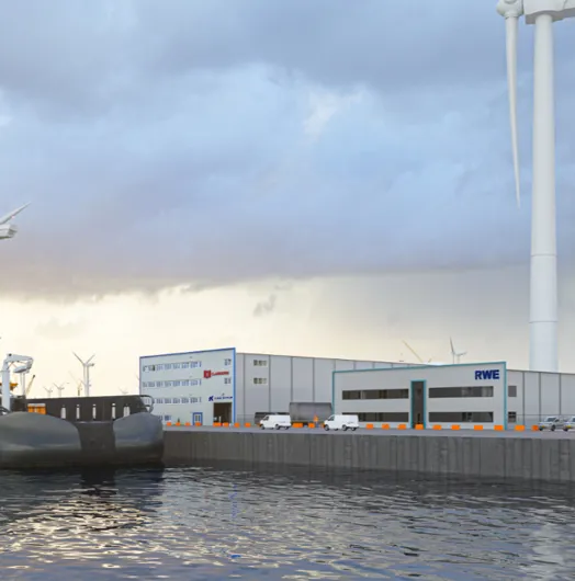 Large ship docked at a port near industrial buildings and wind turbines.