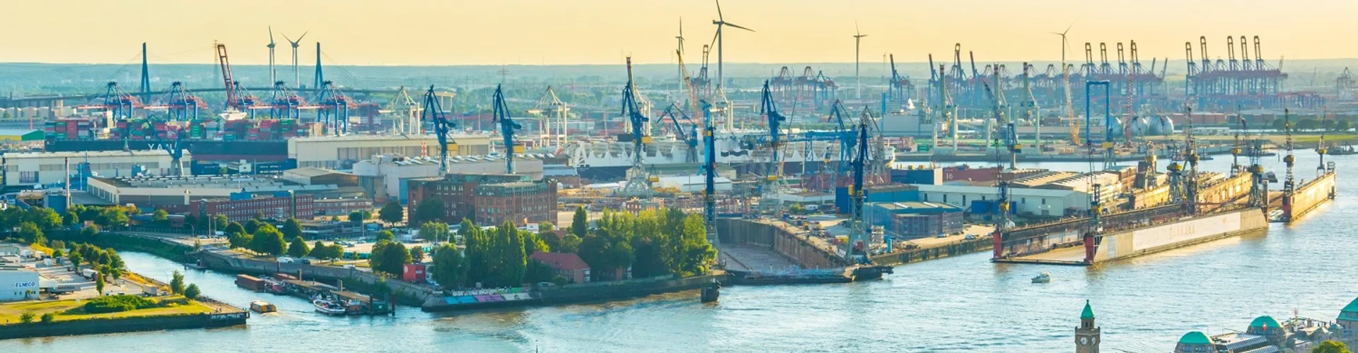 Panoramic view of coastal landscape with lush hills, rocky shoreline, a small town, and moored boats.