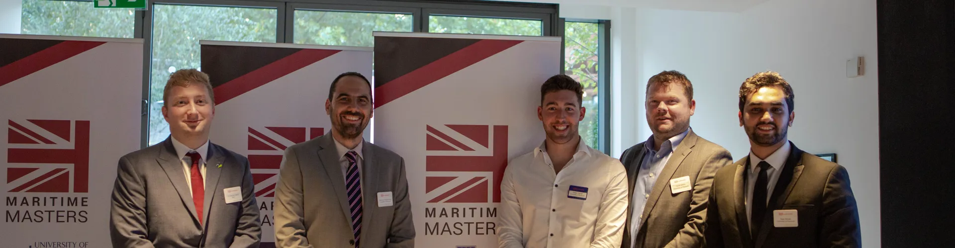 Five men in suits stand by Maritime Masters banners.