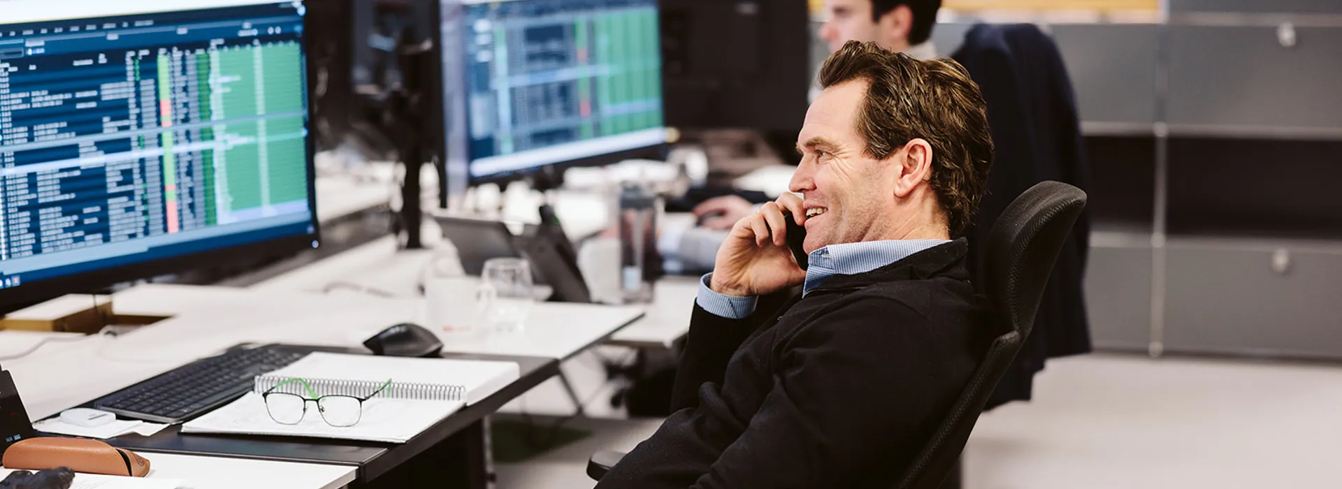 Man on phone in office, monitors with data screens.