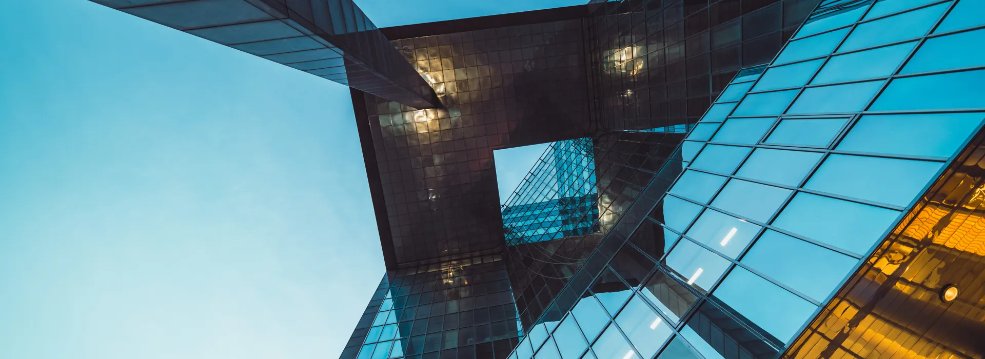 View looking upward at an angular, reflective modern building with glass and metal surfaces.