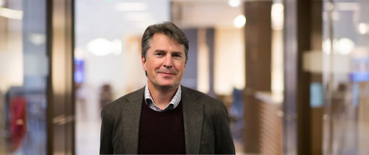 Man in a blazer smiling inside an office.
