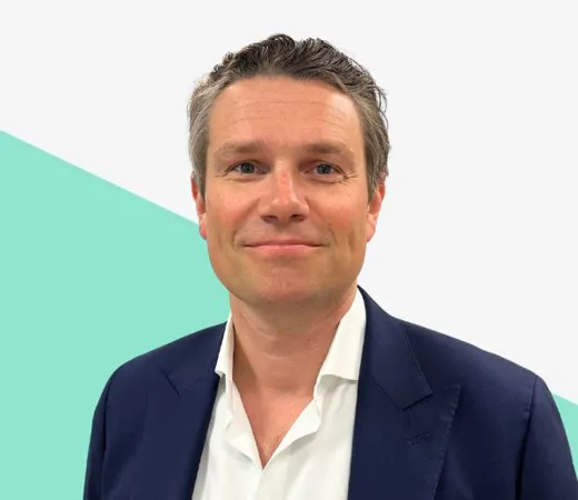 Man with wavy hair in a dark suit jacket, smiling, against a light background with a teal geometric shape.